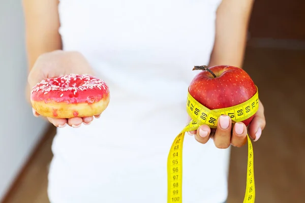 Ernährungskonzept, Frau mit einer Auswahl an schädlichem Donut und frischem Apfel. — Stockfoto