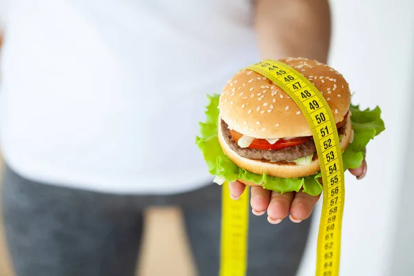 Diet koncept, kvinna som håller skadliga fett burgare med gul måttband. — Stockfoto