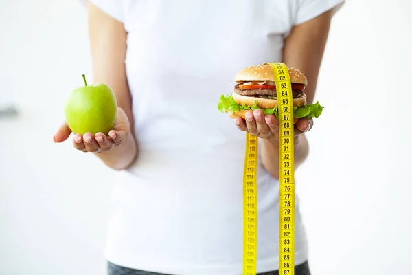 Concepto de la dieta, mujer que sostiene una opción de hamburguesa dañina y manzana fresca. — Foto de Stock