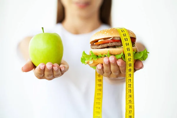 Concepto de la dieta, mujer que sostiene una opción de hamburguesa dañina y manzana fresca. — Foto de Stock