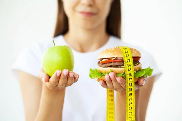 Diet koncept, kvinna som håller ett val av skadlig hamburgare och färska äpple. — Stockfoto