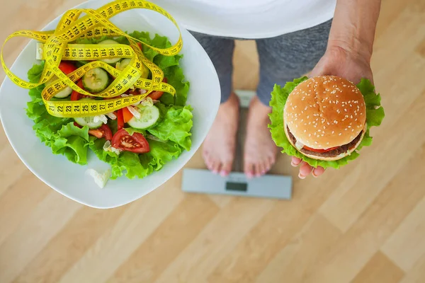 Dietní koncept, žena vybírá mezi nezdravým hamburgerem a čerstvým salátem — Stock fotografie