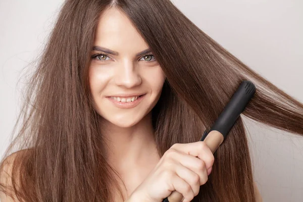 Hermosa mujer endereza su cabello con una rizadora — Foto de Stock