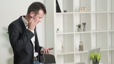 Takım elbiseli genç adam ofiste kulaklıkla müzik dinliyor..