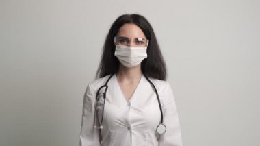Gözlüklü ve maskeli kadın doktor kameraya poz veriyor.
