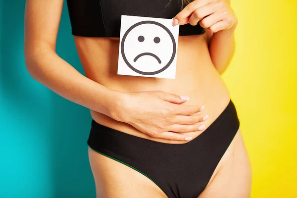 Salud de las mujeres, el cuerpo de las mujeres tiene una tarjeta de una sonrisa triste cerca del vientre — Foto de Stock