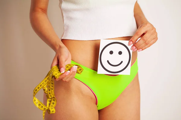 Acercamiento de una mujer con una figura delgada muestra el resultado sosteniendo una tarjeta cerca de su vientre con una sonrisa y una cinta amarilla medida. — Foto de Stock