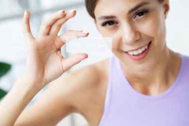 Diş beyazlatıcı, gülümseyen güzel bir kadın elinde beyaz bir şerit tutuyor..