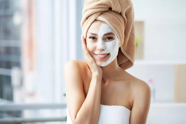 Retrato de cerca de una hermosa chica con una toalla en la cabeza aplicando mascarilla facial — Foto de Stock