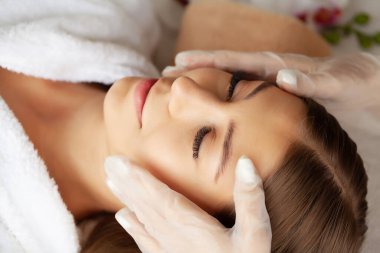 Genç bir kadın spa salonunda yüz masajından hoşlanıyor.