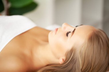 Genç bir kadın spa salonunda yüz masajından hoşlanıyor.