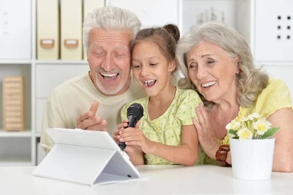 祖父母の孫娘タブレットを自宅でカラオケで歌うと — ストック写真