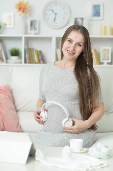 快乐怀孕妇女与耳机在腹部摆姿势在家 — 图库照片