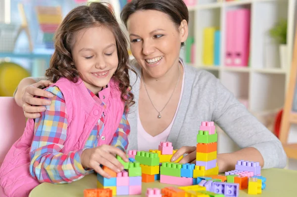 巻き毛の小さな女の子と彼女の母親を自宅にカラフルなプラスチック製のブロックで遊んで — ストック写真