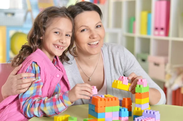 巻き毛の小さな女の子と彼女の母親を自宅にカラフルなプラスチック製のブロックで遊んで — ストック写真