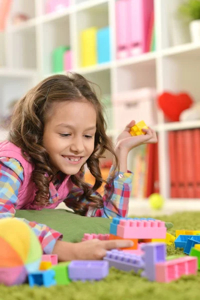 カラフルなプラスチック製のブロックで床に横たわっている間遊んで巻き毛の小さな女の子 — ストック写真