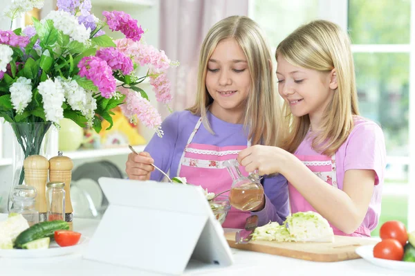 Two Girls Pink Aprons Pouring Oil Salad Kitchen Table Tablet — Stock Photo, Image