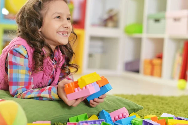 カラフルなプラスチック製のブロックで床に横たわっている間遊んで巻き毛の小さな女の子 — ストック写真