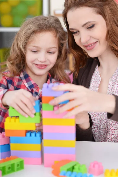 可爱的小女孩和她的母亲在她的房间里玩五颜六色的塑料块 — 图库照片