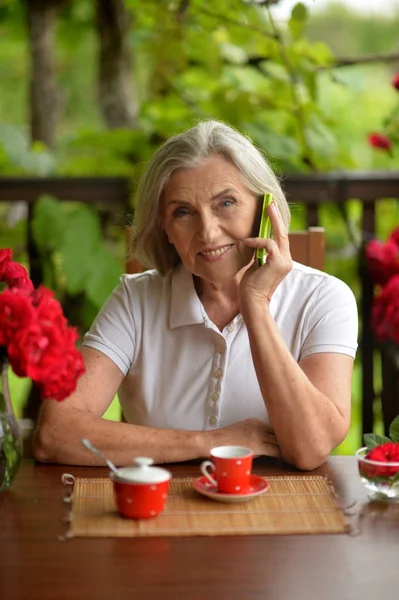 一位快乐的老年妇女在喝咖啡时与智能手机交谈的画像 — 图库照片