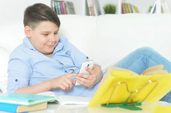 小男孩与智能手机玩游戏在家里 而不是做家庭作业 — 图库照片
