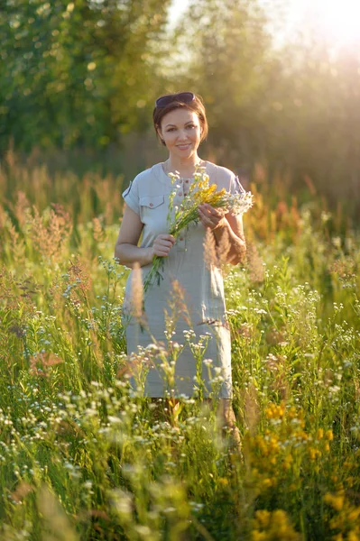 緑の草原に立っている野生の花を持って眺めること若い女性 — ストック写真