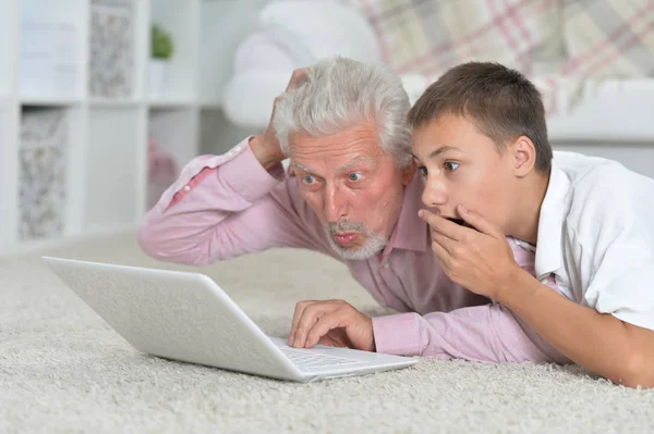 祖父与孙子使用膝上型电脑 而躺在地板上在家 — 图库照片
