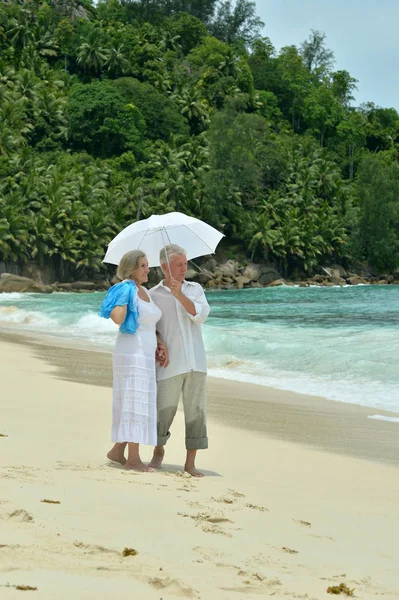快乐的老夫妇休息在热带海滩与伞 — 图库照片