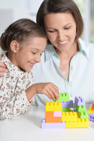 巻き毛の小さな女の子と彼女の母親を自宅にカラフルなプラスチック製のブロックで遊んで — ストック写真