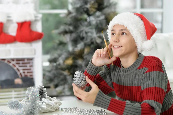 十代の少年がマツ円錐形装飾を着色クリスマスの準備の肖像画 — ストック写真