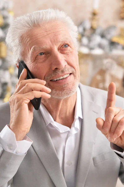 ぼやけているクリスマス ツリーの背景に電話で話している上級ビジネスマンの肖像画 — ストック写真