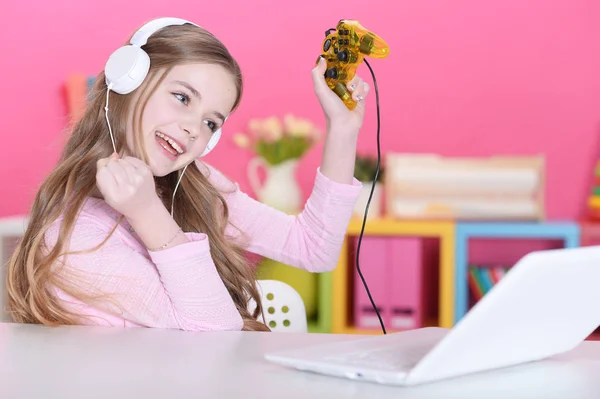 可爱的女孩的肖像玩电脑游戏与笔记本电脑在书桌 — 图库照片