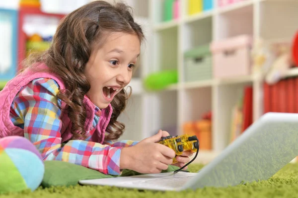 可爱的女孩玩电脑游戏与笔记本电脑 而躺在绿色的地板上在家里 — 图库照片