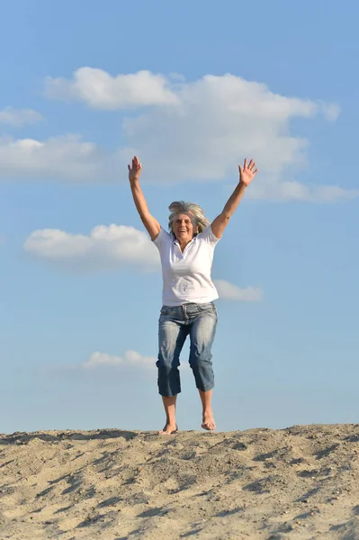 快乐的老年妇女跳在沙滩山上 — 图库照片