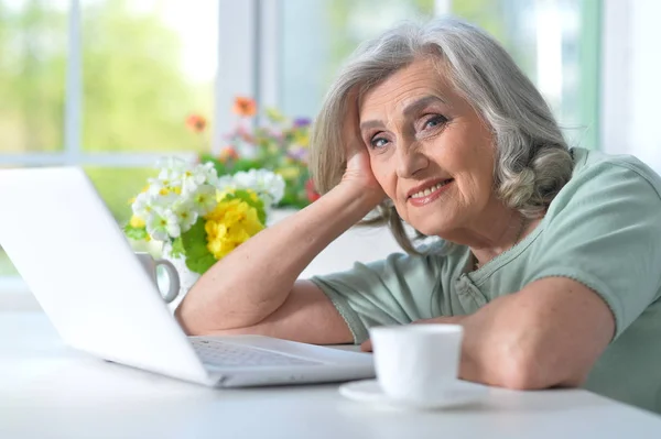美丽的老年妇女使用笔记本电脑 而喝茶 — 图库照片