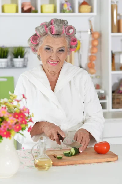 キッチンで料理白のバスローブと髪のカーラーを身に着けている美しいシニア女性 — ストック写真