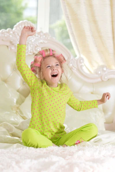 可爱的小女孩与粉红色的卷发有乐趣在床上在家里 — 图库照片