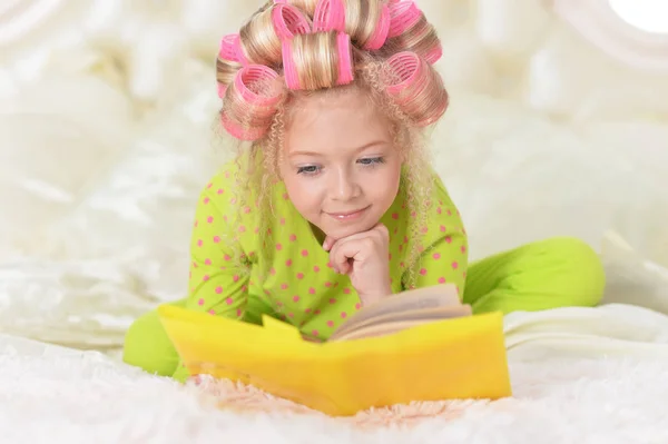 自宅のベッドで本を読んでピンクのカーラーで素敵な女の子 — ストック写真