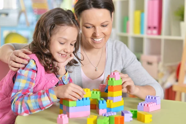 巻き毛の小さな女の子と彼女の母親を自宅にカラフルなプラスチック製のブロックで遊んで — ストック写真
