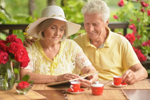 幸福老年夫妇读书 而在家里的露台上喝咖啡 — 图库照片