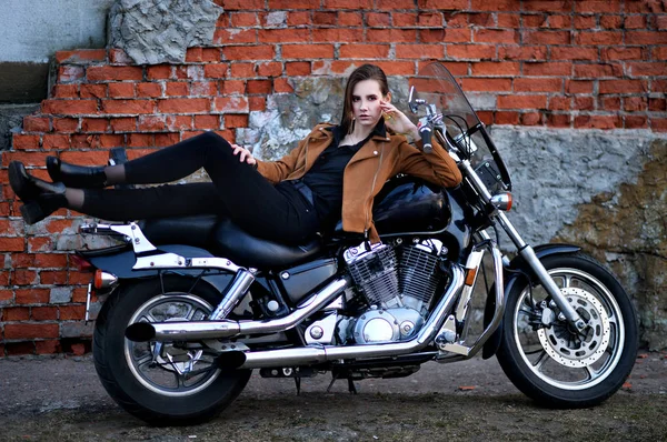 レンガの壁の近くでオートバイでポーズをとる美しい若い女性 — ストック写真