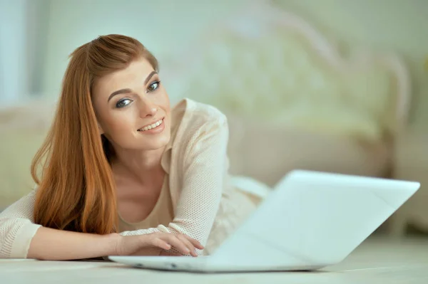 Young woman lying on floor with laptop — Stock Photo, Image