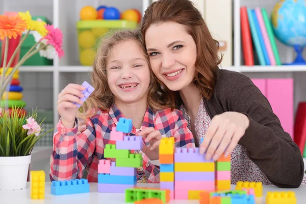 かわいい女の子と彼女の母親が彼女の部屋でカラフルなプラスチック製のブロックを一緒に遊んで — ストック写真
