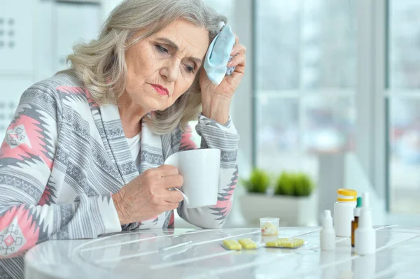 悲伤生病的资深妇女坐在桌前吃药 — 图库照片