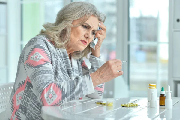 悲伤生病的资深妇女坐在桌前吃药 — 图库照片