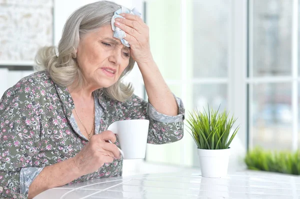 生病的老年妇女坐在家里的桌子 — 图库照片