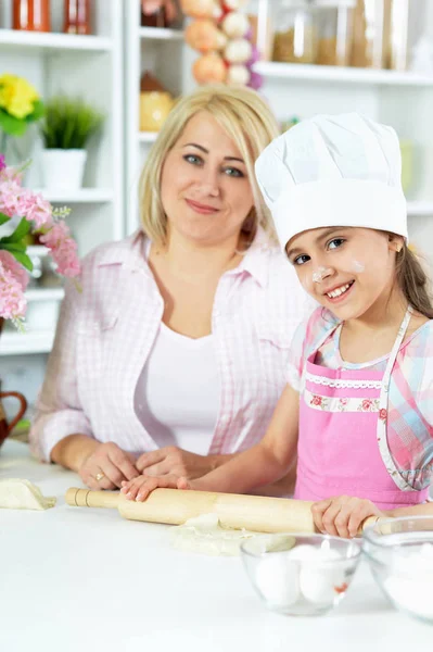 可爱的女孩在白色帽子与她的母亲在厨房里做面团在家 — 图库照片