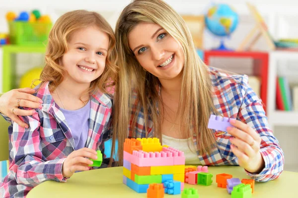 かわいい女の子と彼女の母親が彼女の部屋でカラフルなプラスチック製のブロックを一緒に遊んで — ストック写真