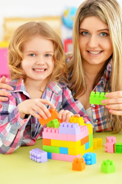 かわいい女の子と彼女の母親が彼女の部屋でカラフルなプラスチック製のブロックを一緒に遊んで — ストック写真