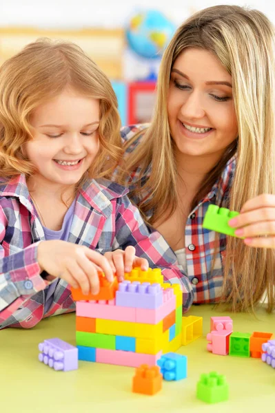 かわいい女の子と彼女の母親が彼女の部屋でカラフルなプラスチック製のブロックを一緒に遊んで — ストック写真